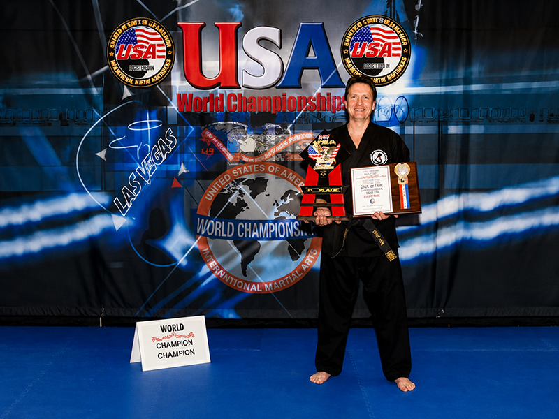 Grandmaster John Gill holding his USA World Championships first-place trophy and Hall of Fame plaque