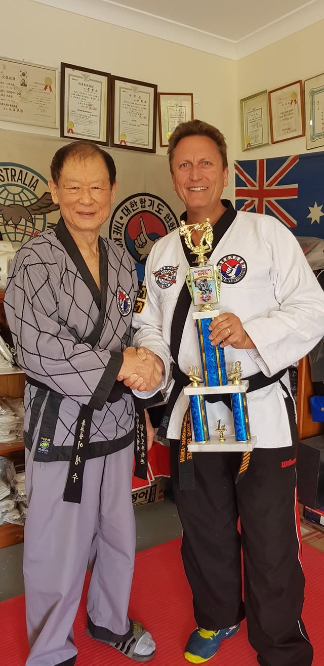Grandmaster John Gill holding the 2018 Australian Open first-place trophy with his Korean Grandmaster