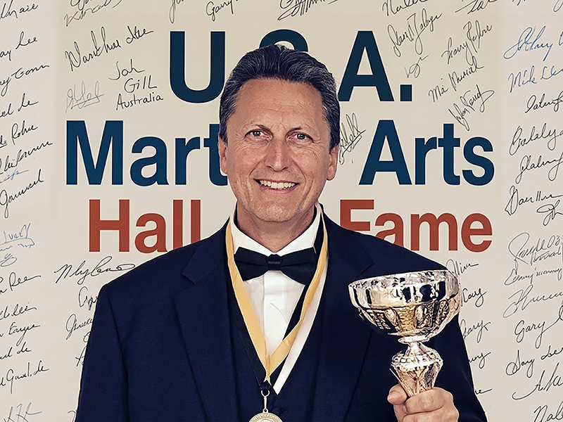 Grandmaster John Gill in a tuxedo holding his trophy at the U.S.A. Martial Arts Hall of Fame